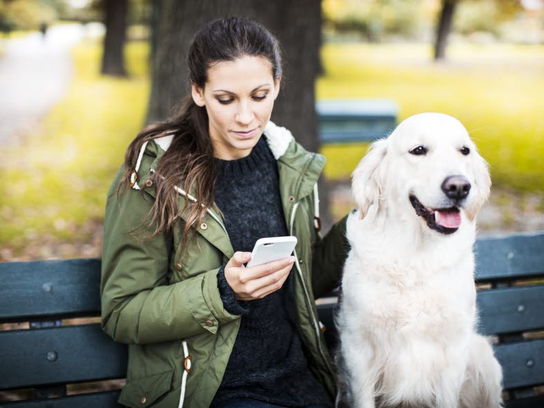 Kvinna sitter på en parkbänk bredvid en hund.