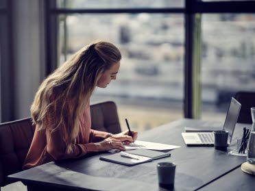 Kvinna sittandes vid ett skrivbord och skriver på ett papper.
