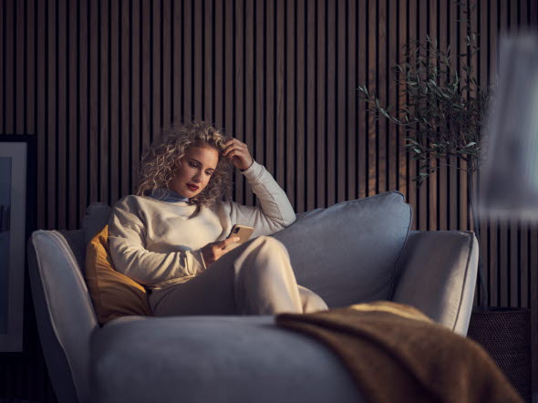 Kvinna sitter i en soffa och tittar i sin mobil