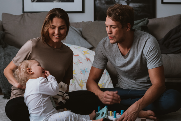 Bild på en leende familj som leker med ett litet barn i sitt vardagsrum.