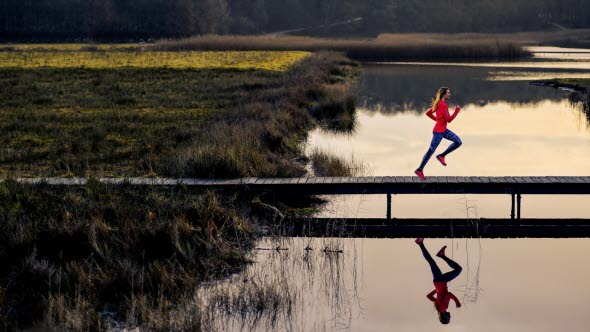 Kvinna joggar över bro ute i naturen