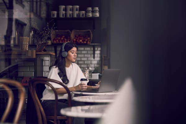 Kvinna med hörlurar som dricker kaffe på ett café med sin laptop på bordet
