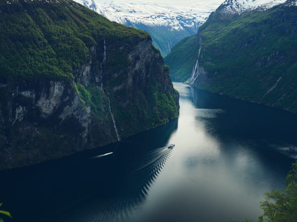 Båt åker genom fjord med höga berg runt omkring.