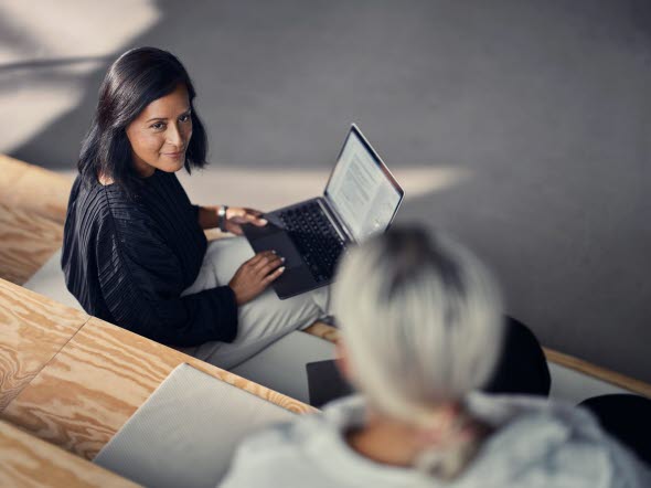Två kvinnor sitter med sina laptops i knät och pratar med varandra om valutakonto.