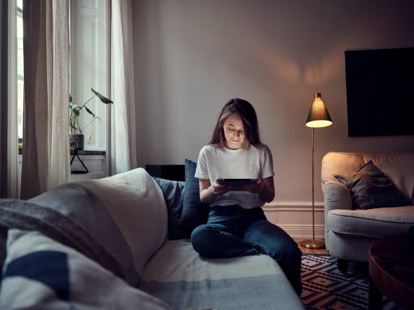 Kvinna som sitter i en soffa och läser på sin tablet om hur man köper bostad