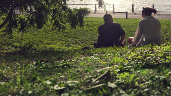 Två personer sitter i gräset vid en flod.
