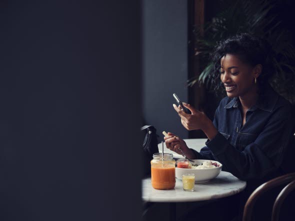 Bild på en kvinna som sitter vid ett matbord och tittar på sin mobiltelefon.