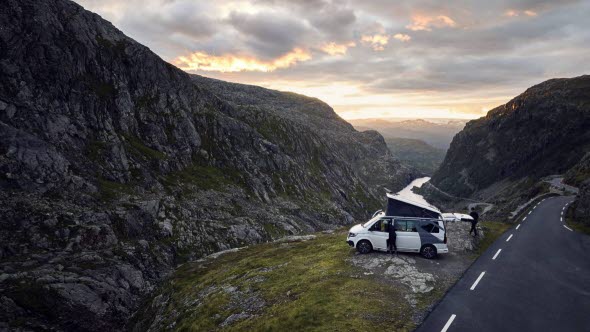 Bil parkerad framför utsikt över höga berg och en fjord.
