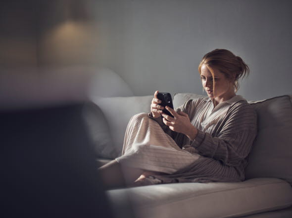 Kvinna som sitter i en soffa och läser på om fonder i sin mobiltelefon.