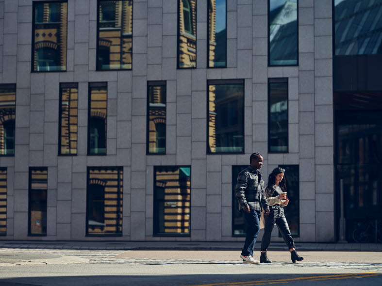 Man och kvinna promenerar framför futuristiskt höghus.