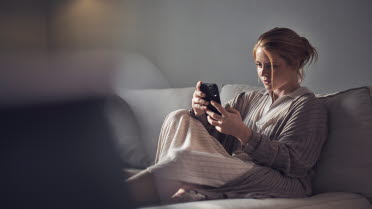 Kvinna sitter i en soffa och tittar på sin mobil