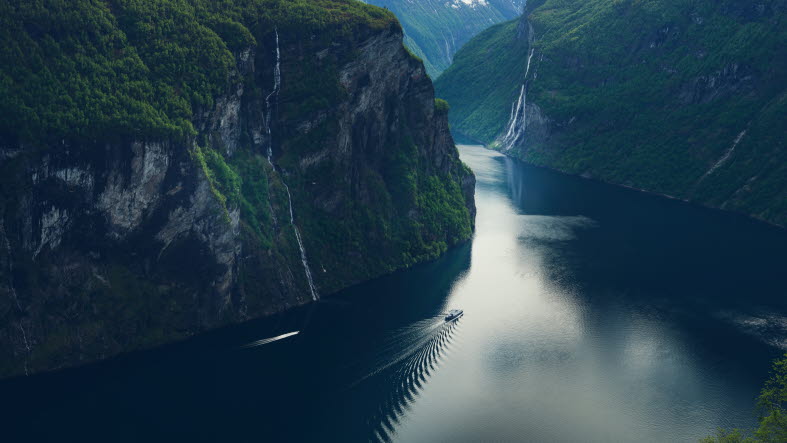 Båt åker genom fjord med höga berg runt omkring.