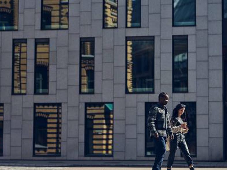 Man och kvinna promenerar framför futuristiskt höghus.