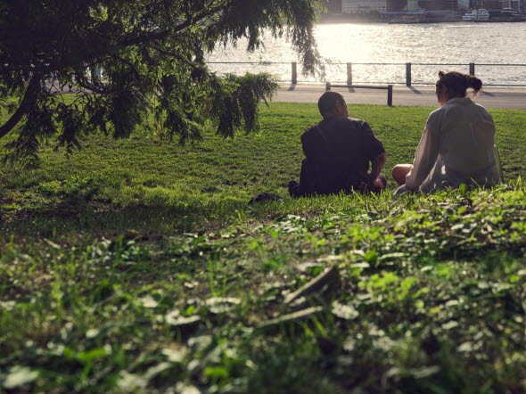 Två personer sitter i gräset vid en flod.