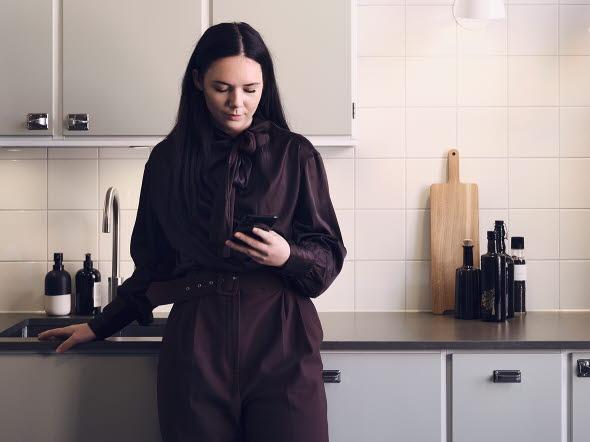 Kvinna som står i sitt kök och tittar på sin mobil