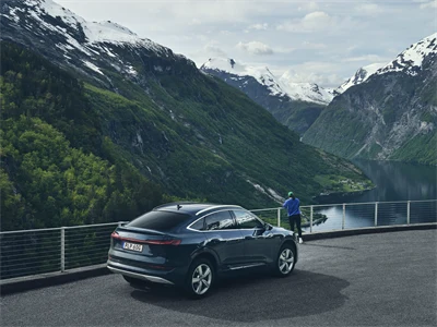 Bil parkerad framför utsikt över höga berg och en fjord.