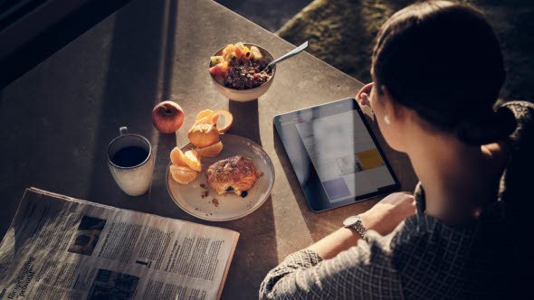 Kvinna läser på tablet vid köksbordet