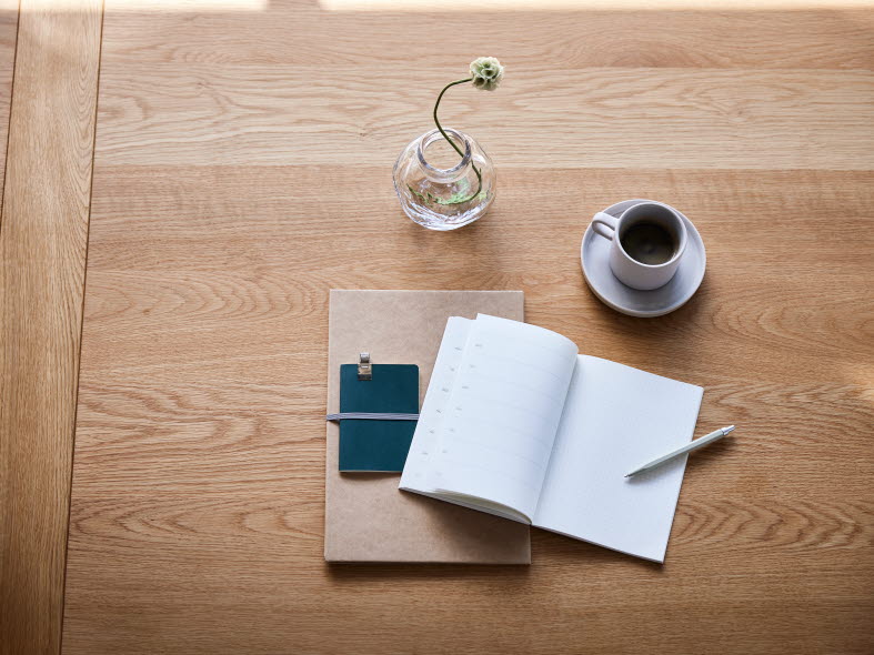 Ett skrivblock, penna och kaffekopp på ett träbord sett uppifrån.