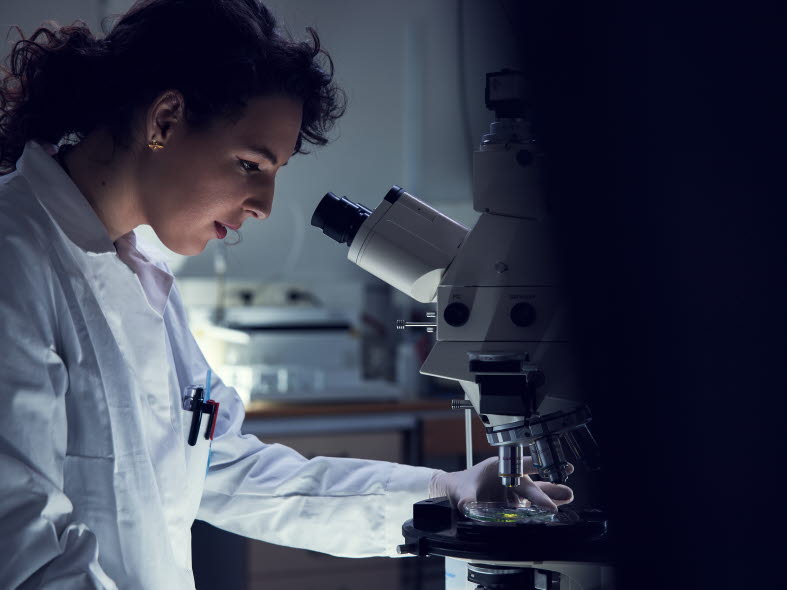 Kvinna i ett laboratorium tittar i ett mikroskop.