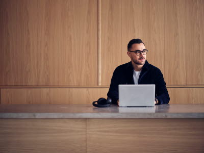 Man i glasögon sitter och arbetar på sin laptop.