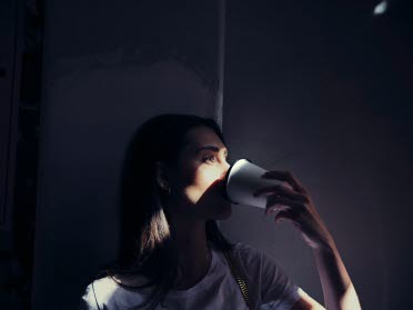 Kvinna som dricker kaffe med en strimma av solljus i ansiktet.