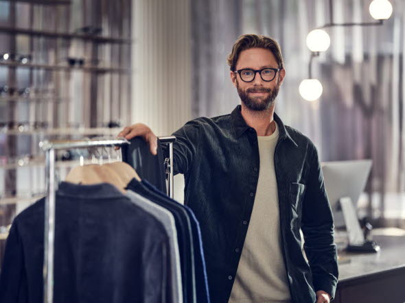 Man som står i en modern butik med kläder på en klädstång.