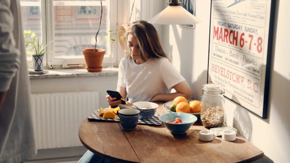 Kvinna vid frukostbord som håller i en mobiltelefon.