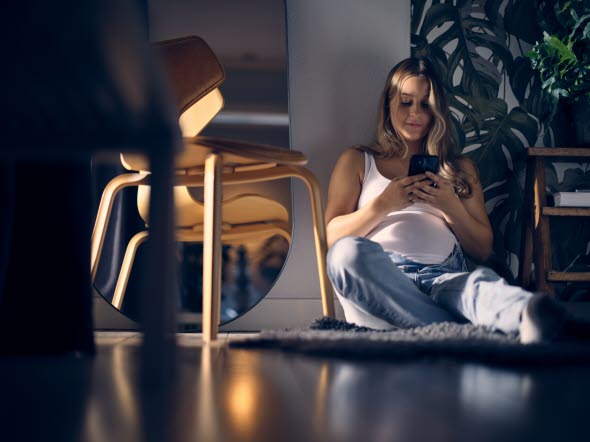 Ung gravid kvinna sitter på golvet och läser på en mobil. 