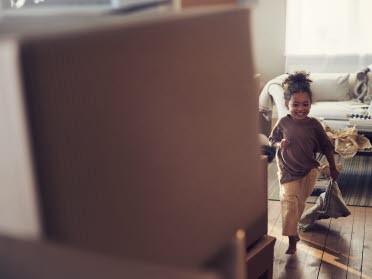 Litet barn springer leende i ett rum med flyttlådor.