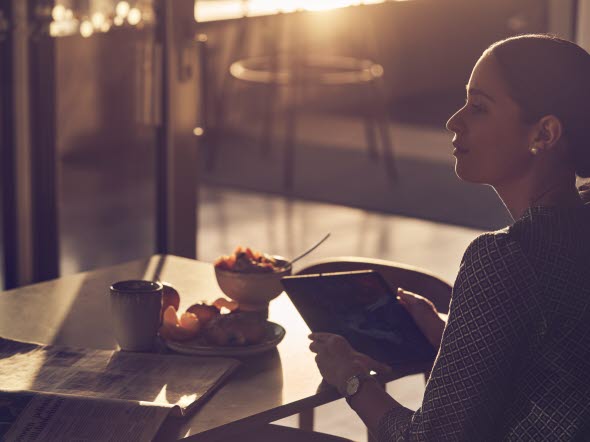 Kvinna sitter på ett fik och äter frukost och använder sin ipad