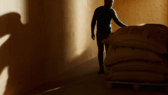 Bild på Rebu Burubwa vid säckar av kaffebönor, grundare till Rutasoka Coffee.